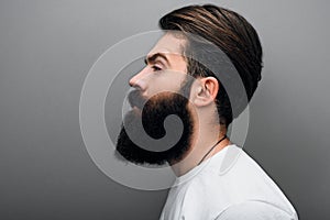 Side view of masculine Caucasian bearded male wearing casual white t-shirt on gray background. Bearded European man model with