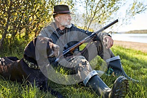 Side view on Mature caucasian hunter sitting with dog on grass