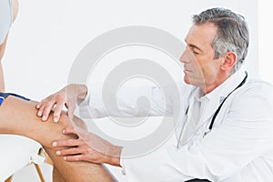 Side view of a mature doctor examining patients knee