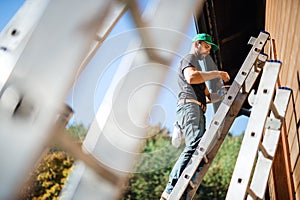 A side view of mature man outdoors in summer, painting wooden house.