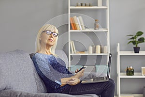 Side view of a mature older woman making phone calls and checking work chats on her laptop.