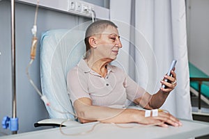 Side view mature woman using smartphone during IV drip treatment