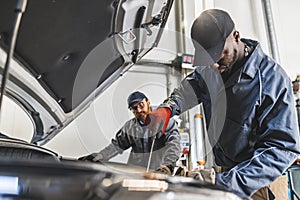 side view of a mechanic working on a car engine and his co-worker looking at him, auto repair shop