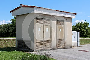 Side view of medium size local electricity substation building with metal front doors next to small grey plastic electrical box