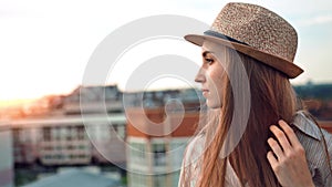 Side view melancholic woman in hat enjoying city landscape at amazing sunset on roof or balcony