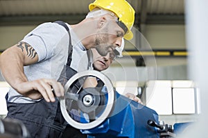 Side view of mid adult worker with colleague operating machinery in industry