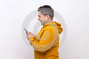 Side view of middle aged man using mobile phone with happy expression, addicted to smartphone.