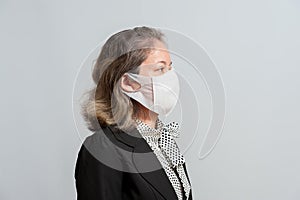 Side view of middle aged mixed race woman in formal wear wearing white surgical mask for protection against coronavirus COVID-19