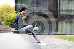 Side view of middle eastern young man using laptop outdoors