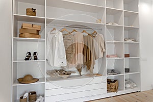Side view on minimalistic modern scandinavian white wood walk in closet with wardrobe in neutral beige colors