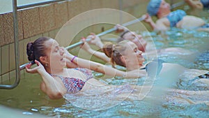 Side view - mixed race people lie in swimming pool with water during exercises on aqua aerobics