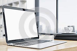 Side view of modern designer office desktop with empty white mock up laptop screen, coffee cup and other items on blurry office
