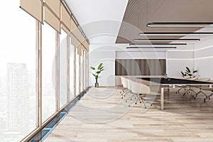 Side view of modern light meeting room interior with office desk and chairs, plant, panoramic window with city view, wooden floor