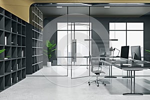 Side view on modern spacious coworking office with black walls and furniture, modern computers, light concrete floor and glass