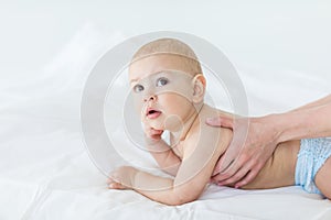 Side view of mother massaging adorable baby boy lying on bed