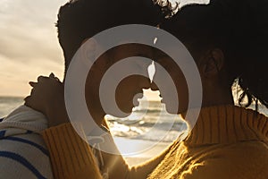 Side view of multiracial couple romancing while hugging each other at beach during sunset