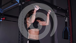 Side view of muscular adult sportswoman in black leggings and bra hanging on metal bar in gym and determinated doing