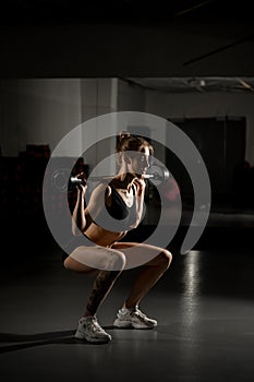 Side view of muscular girl performing squat exercises with barbell weight in 15 kilograms in modern gym
