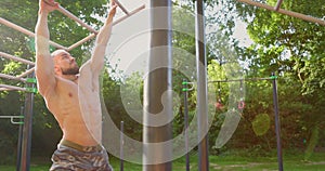 Side view of muscular man shirtless swinging exercising on monkey bar at sports ground in park. Fitness sport traning on