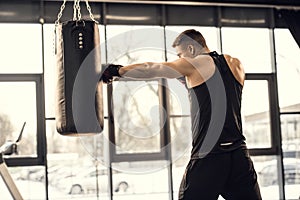 side view of muscular young boxer training with punching bag