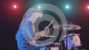 Side view of musician in a festive shark costume plays drums and hits percussion cymbals. A musician plays at a festive
