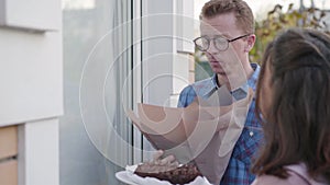 Side view of nervous redhead Caucasian man in eyeglasses knocking the door. His fiancee standing next to him with a