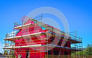 Side view of a new two-storey detached house under construction covered by red protective layer