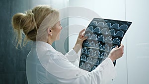 Side view of nice blonde doctor in white lab coat looking at MRI film