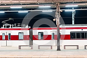 Side view of the night time station platform and commuter train in the parking lot.