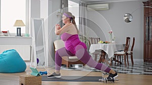 Side view of obese woman trying to do twine working out training at home. Motivated happy Caucasian fat lady turning to