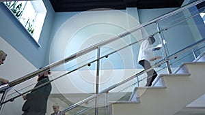 Side view office stairs with busy people walking up and down. Concentrated confident Caucasian and African American men