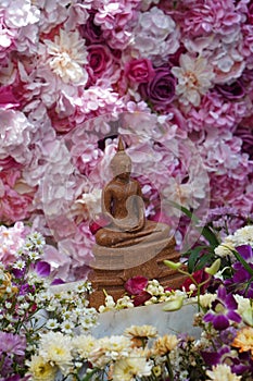 side view old brown buddha statue in front flowers, blur wall flowers and roses colorful background, worship, banner, template,