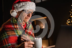 Side view of old man drinking cocoa with marshmallows on christmas eve, Elderly man in santa hat alone watching movie on