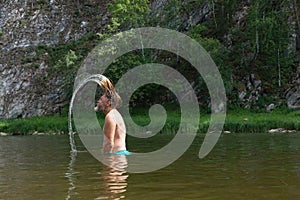 Side view of old man standing waist-deep in the mountain river and throwing his long wet hair back. Tourism, active leisure, bath