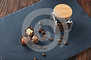 Side view of overturned glass jar with coffee beans and chocolate candies on wooden background, selective focus