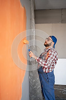 Side view of painter man painting the wall, with paint roller on big empty space