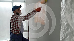 Side view of a painter painting a wall with a paint roller. Home renovation and remodeling concept