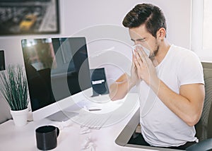 Side view of the patient's employer. sneezing into a tissue in an office near the window in the computer. Freelancer photo
