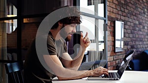 Side view of pensive young man programming on laptop sitting at desk at home office.