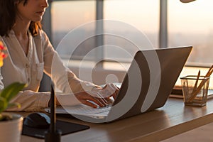 Side view photo of a female programmer using laptop, working, typing, surfing the internet at workplace.