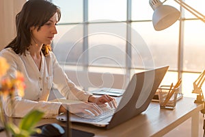 Side view photo of a female programmer using laptop, working, typing, surfing the internet at workplace.