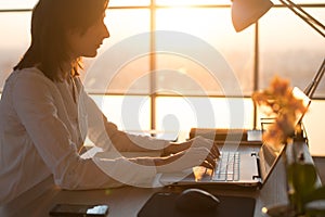 Side view photo of a female programmer using laptop, working, typing, surfing the internet at workplace.