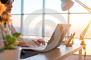 Side view photo of a female programmer using laptop, working, typing, surfing the internet at workplace.