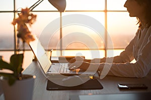 Side view photo of a female programmer using laptop, working, typing, surfing the internet at workplace.