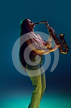 Side view photo of Indian woman, saxophonist performing solo in neon light against gradient background.