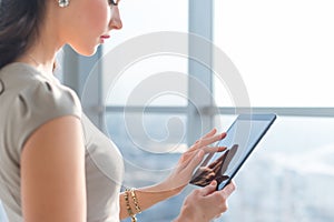 Side view photo of young female teleworker using tablet, searching and browsing information via wi-fi connection