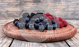 Side view of a pile of ripe red, blue and black berries laying in wooden plate