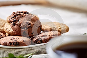 Side view of a plate of chocolate chip cookies on a white plate on homespun tablecloth, selective focus