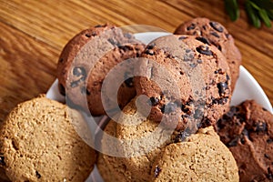 Side view of a plate of chocolate chip cookies on a white plate on wooden background, selective focus