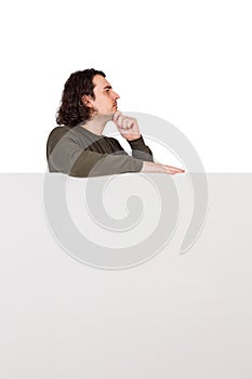 Side view of pondering young man, stands behind a blank banner, looks ahead thoughtful. Empty sheet with copy space for